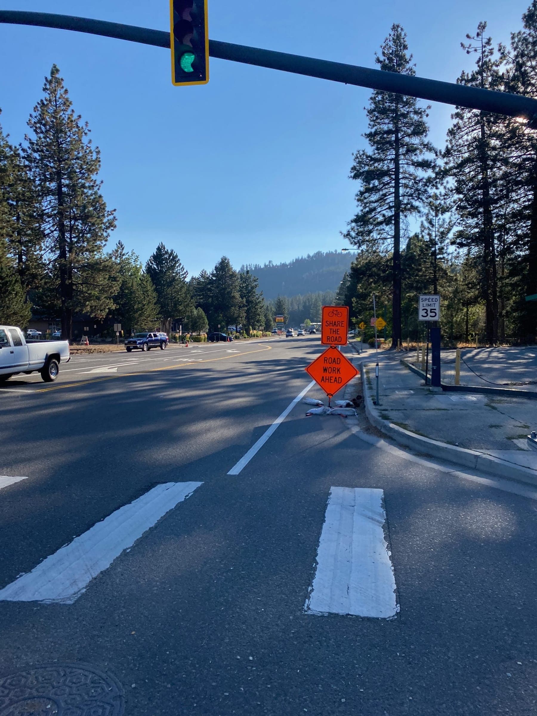 A “Share the Road” sign beside a road-work sign at a signalized crosswalk on a Tahoe street